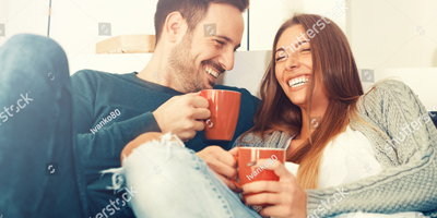 Photo of a couple sitting on the couch laughing and drinking coffee. This photo represents how couples therapy in Georgia can help improve your relationship and strengthen your bond with your partner. Click here to learn more!