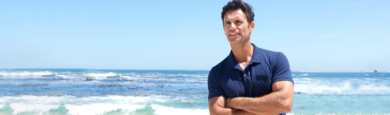 Photo of a man standing on the beach on a sunny day with his arms crossed. This photo represents how enmeshed men in Georgia can begin creating healthy boundaries in their relationships.