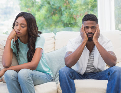Photo of an African American couple sitting on a couch sitting away from each other looking upset. Are you and your partner tired of fighting? Learn how discernment counseling in Georgia can help you and your partner discover if your relationship will last.