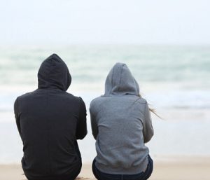 Photo of a couple sitting on a beach wearing hoodies while facing the ocean on a cloudy day. Is there conflict in your relationship? Learn how eft in Georgia can help you and your partner manage conflict.