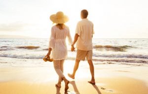 Photo of a couple walking happily down the beach holding hands during sunset. Learn how you can manage your emotions with EFT therapy in Georgia.