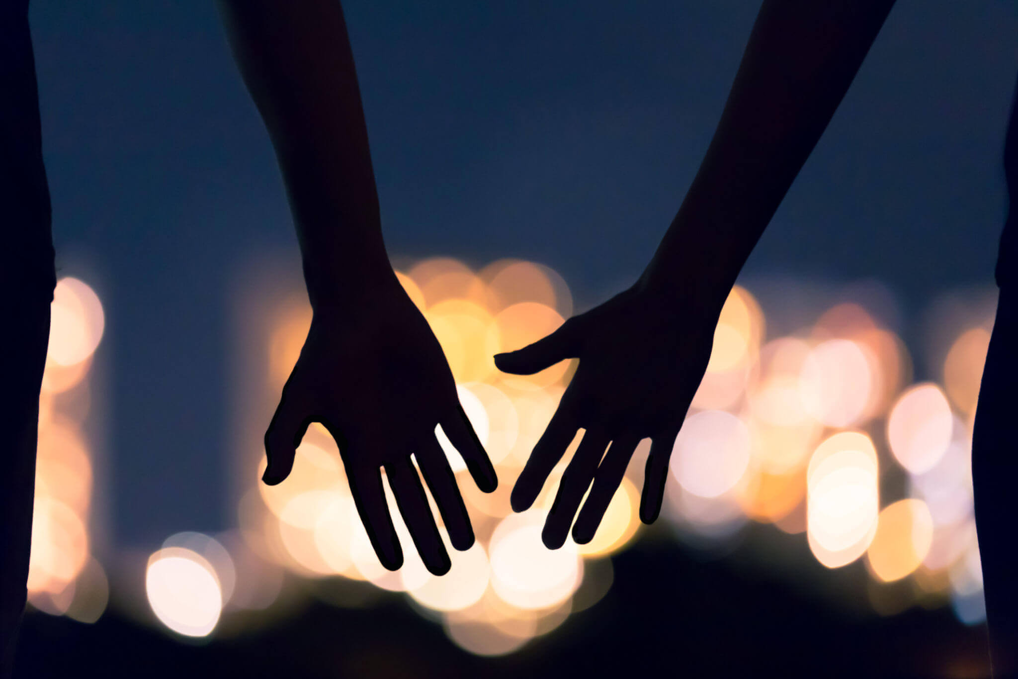 Photo of a couple reaching for each others hands at night. Are you struggling with deciding if you want to continue with your relationship? Learn how discernment counseling in Georgia can help provide you support.