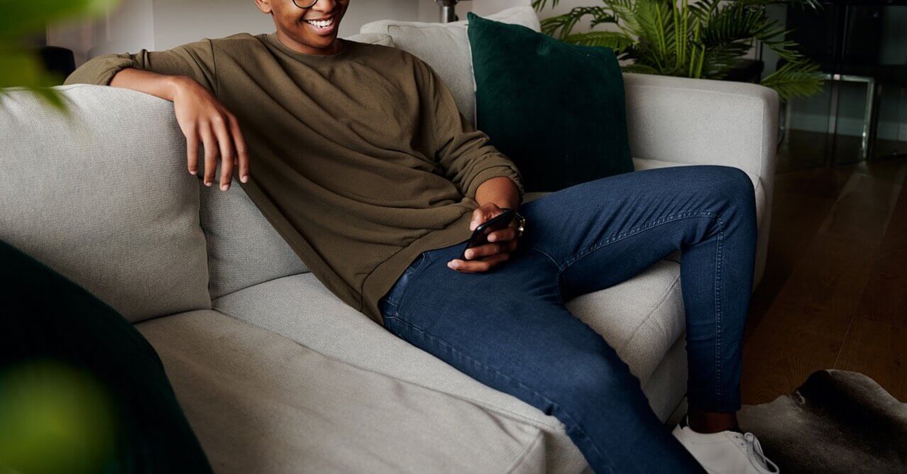 Photo of a young black male casually sitting on a couch smiling. This photo represents how depression counseling in Georgia can help you recover from your depression symptoms. Learn from a depression therapist in Georgia how to begin treatment.