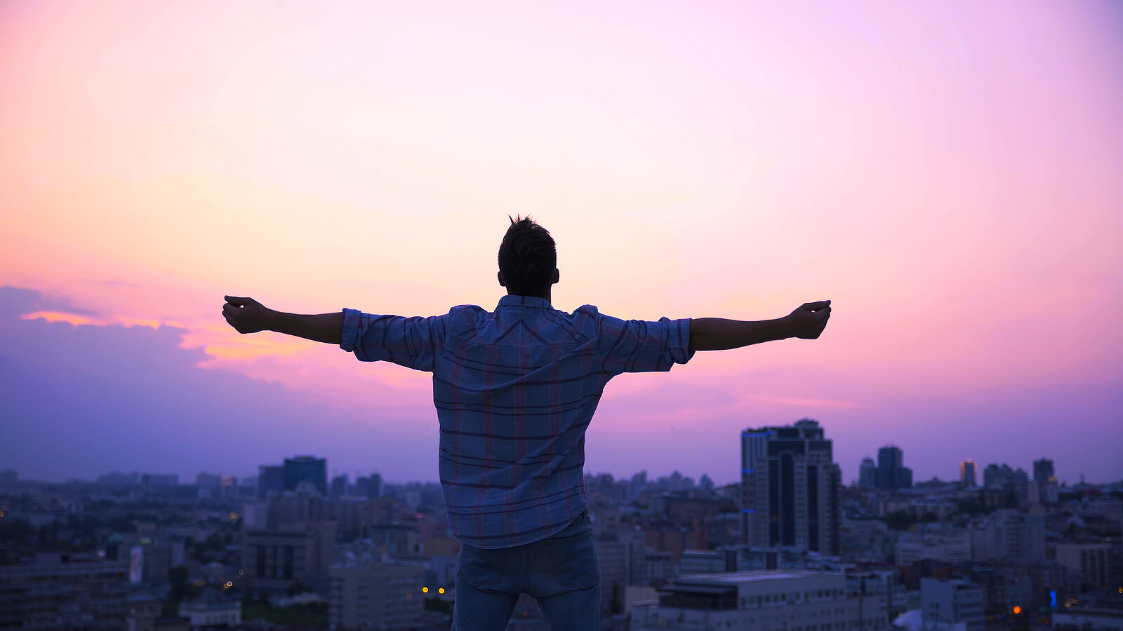 Photo of a man standing on a roof with his arm outstretched feeling free with a purple and pink sunset sky. Break free from your sexual addiction. Meet with a skilled therapist to recover with sexual addiction therapy in Georgia.