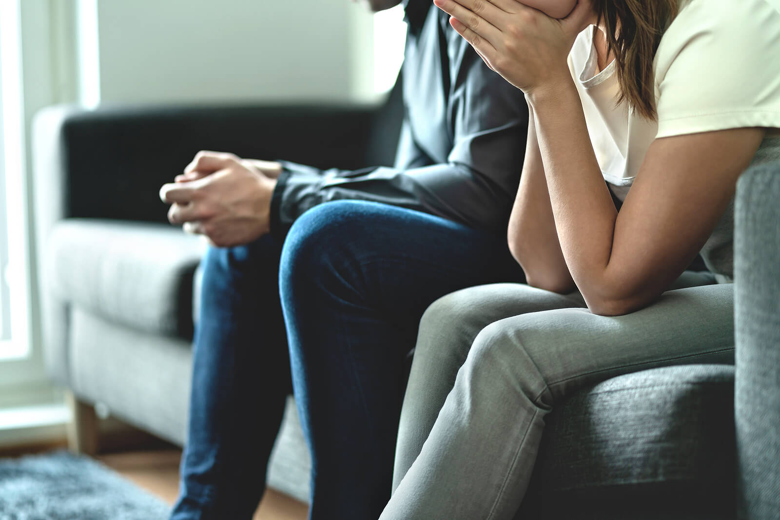 Photo of a couple sitting on a couch with the woman holding her hands to her mouth looking upset. Are you struggling with infidelity? Learn from a therapist how betrayal trauma in Georgia can affect your relationship.