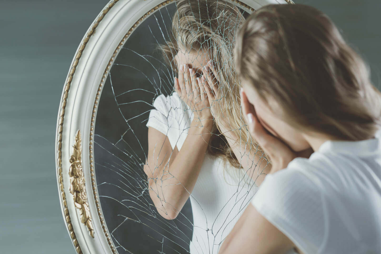 Photo of a young woman standing in front of a cracked mirror covering her face in her hands looking upset. Are you struggling with anorexia? If you're looking for support, learn how anorexia nervosa treatment in Georgia can help you recover.