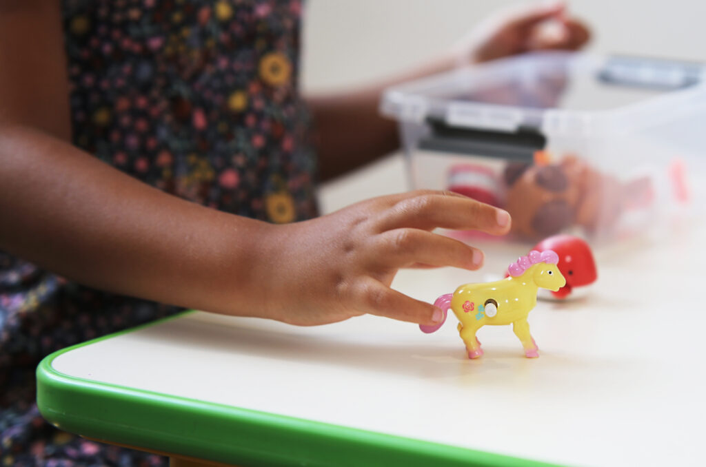 Child's hand hovering over toy pony during play therapy for kids